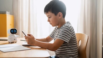Young boy using a smartphone app to control an educational robot at a desk. Child learning STEM and coding at home. Modern technology concept - Powered by Adobe