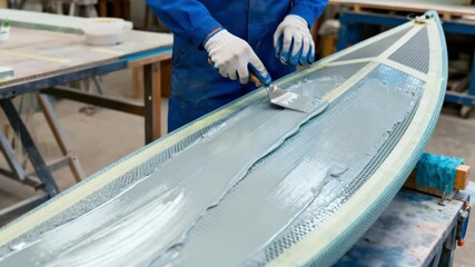 Worker smoothing a fiberglass boat hull mold with epoxy layers focusing on skillful molding techniques and the creation of durable marine structures.