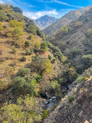 Genil river flows through a rocky gorge surrounded by colorful vegetation in the Sierra Nevada National Park in Andalusia, Spain, framed by towering mountain peaks along Verada de la Estrella path.