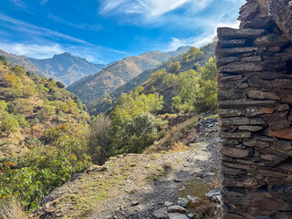 Ancient stone ruins of Cortijo del Hornillo stand against dramatic backdrop of high peaks in Sierra Nevada, Spain, offering a historic view for hikers exploring the mountains of Andalusia in autumn.
