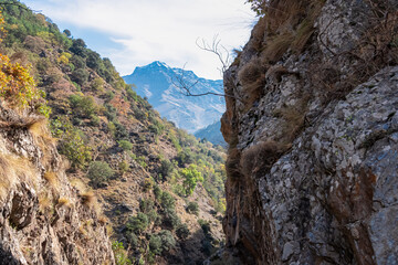 Steep rocky cliffs frame a breathtaking view of the La Alcazaba peak rising above the deep valley, captured along the scenic Vereda de la Estrella hiking route in Granada, Andalusia, Spain.