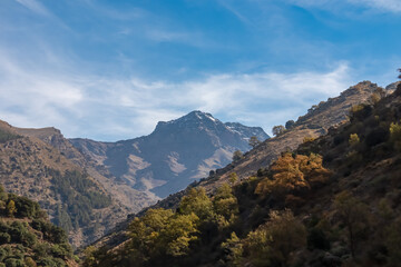 Majestic view of the snow-capped La Alcazaba peak rising above the steep scenic valley slopes, captured during a sunny autumn hike on the Vereda de la Estrella in Granada, Andalusia, Spain.