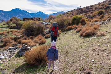 A mother with a baby carrier and a girl hike the Vereda de la Estrella, admiring the autumn foliage and snow-capped peaks of the Sierra Nevada mountains in Andalusia, Spain on a sunny day.