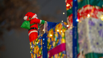 Small Santa Claus figure attached to colorful gift boxes with festive lights
