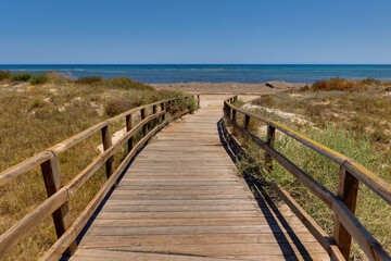 Obraz premium Wooden Boardwalk Leading to a Sunny Beach and Blue Sea