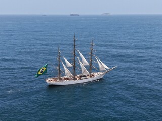 Aerial view of a three-masted sailing ship with sails and a large Brazilian flag on the stern sailing in the Atlantic Ocean. The training ship of the Brazilian Navy.