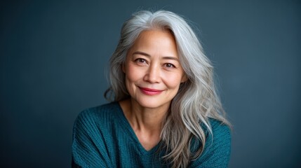 A warm and inviting portrait of an elegant senior woman with flowing silver hair, embodying grace and wisdom against a serene gray backdrop, celebrating the beauty of aging.