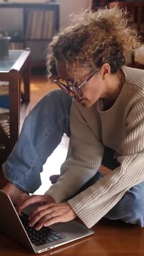Middle-aged woman using laptop at home, sitting or lying on floor, relaxed and chill, working or browsing, smart working, remote work freedom, enjoying leisure and technology, modern lifestyle