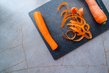 Freshly peeled carrot with vibrant orange ribbons falling onto a cutting board
