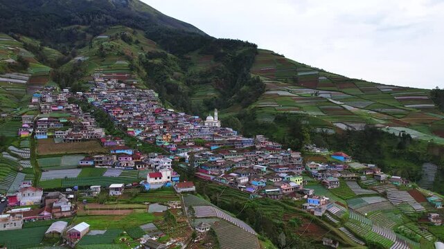 Aerial drone footage of the famous Nepal Van Java village, on the slope of Sumbing volcano, in Magelang area, Java island, Indonesia, in a white cloudy atmosphere, and many vegetable fields behind
