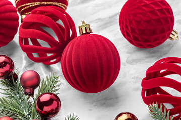 Christmas ball ornaments, red velvet baubles, and pine branches on marble table