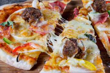 Close-up of freshly baked pizza slices being pulled apart with melted cheese stretch, topped with...