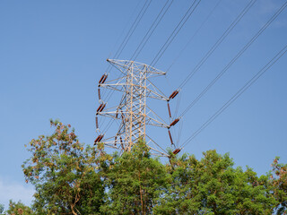 High-voltage power poles and cables in the middle of the forest, steel lattice transmission towers for electricity distribution. Industrial infrastructure concept.