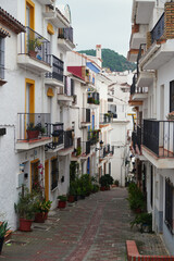 picturesque narrow street in the white village of Oj&eacute;n, Spain. The image shows traditional Mediterranean architecture with whitewashed walls, iron balconies, and steep cobblestone paths