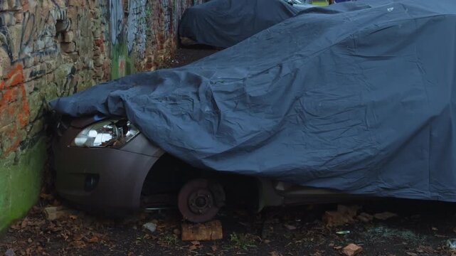 Rusty sedan lacks front wheel, Old sedan partially hidden with missing wheel and rusty brake components