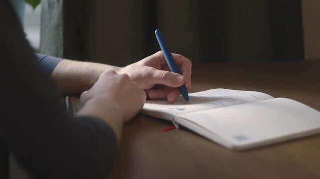Woman writing with her left hand in a notebook at a wooden table, close-up, practicing left-handed writing, business and learning.