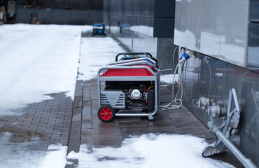Portable red gasoline generator providing backup power to a modern building on a snowy winter day.