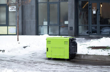 Silent green portable diesel generator providing emergency power on a snowy city street near an office building.