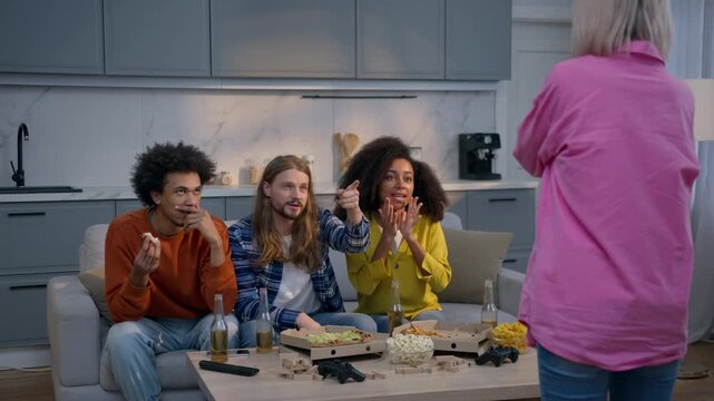 Four multiethnic friends men women playing pantomime game home party having fun smiling together Caucasian woman showing gesture African American guys guess charades friendship funny activity indoor