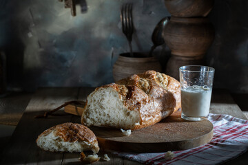 Fresh wheat bread and milk in a glass on a rustic table