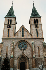 Obraz premium Catholic cathedral with twin towers in Sarajevo during early morning. Symmetrical facade and soft light express religious heritage, historical architecture, and peaceful city mood.