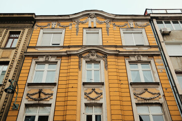 Obraz premium Yellow historic building facade with ornate stucco details and tall windows in morning Sarajevo. Classical architecture reflects urban heritage and calm atmosphere of the old city.