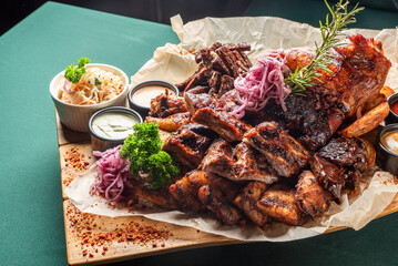 A large, appetizing platter of assorted grilled meats, including ribs, a pork knuckle, and various...