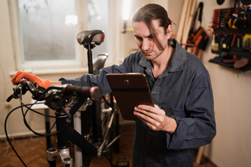 Bicycle repair concept. maintenance in workshop. mechanic man using tablet in startup for restoration.
