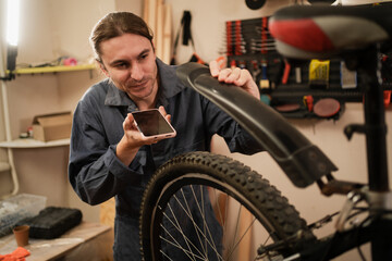 Mechanic wearing workwear recording voice message repairing bicycle in workshop
