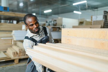 African american Carpenter moving wooden planks in furniture factory