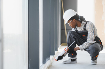 Construction worker sealing window frame in building under construction
