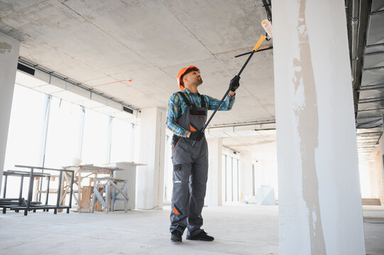 Construction worker painting walls and ceiling with telescopic paint roller