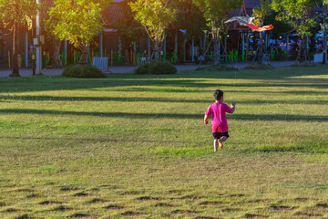 Happy young boy running across grassy field and pulling string of colorful kite. A young child having fun flying kite on windy day in open green space. Joyful moment of childhood play and freedom.