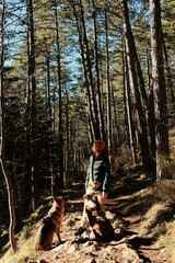 Fototapeta premium A woman stands on a forest trail with two dogs during a quiet hike. Outdoor lifestyle scene shows companionship, trust, and emotional connection between a woman and her dogs in nature.