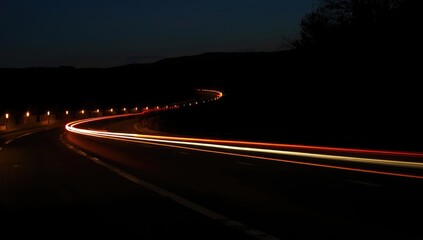 Nighttime street illuminated by passing vehicle headlights creating light streaks, ideal for urban environment backgrounds or traffic safety visuals