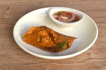 grilled curry fish and egg horseshoe crab wrapped in banana leaf dipping spicy chili sauce on plate