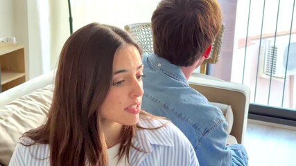 Young couple sitting back to back on sofa at home during relationship conflict, woman facing camera while man turns away, emotional tension, communication breakdown, trust issues and intimate domestic