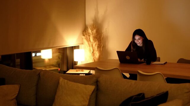 Eva at home at night sitting on sofa using laptop under warm lamp light, making a video call or online meeting for work or leisure, relaxed evening lifestyle, modern technology remote communication