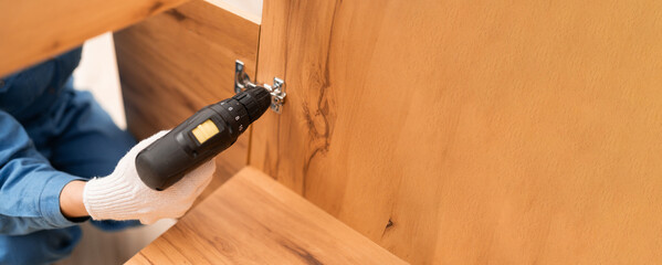 Close-up of screwing in a furniture hinge with electric drill. Master Installing a furniture door hinge