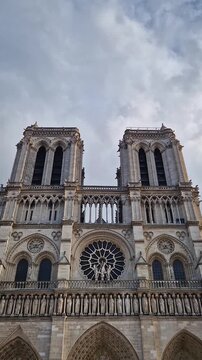 The Notre-Dame Cathedral facade in Paris, France, highlighting the intricate portals, the Gallery of Kings, the iconic rose window and two massive bell towers against a dramatic sky