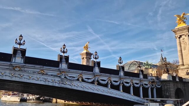 View from a cruising boat trip along the Seine river to the breathtaking Pont Alexandre III in Paris, France. The bridge is adorned with gilded statues. The Grand Palais with glass dome in background