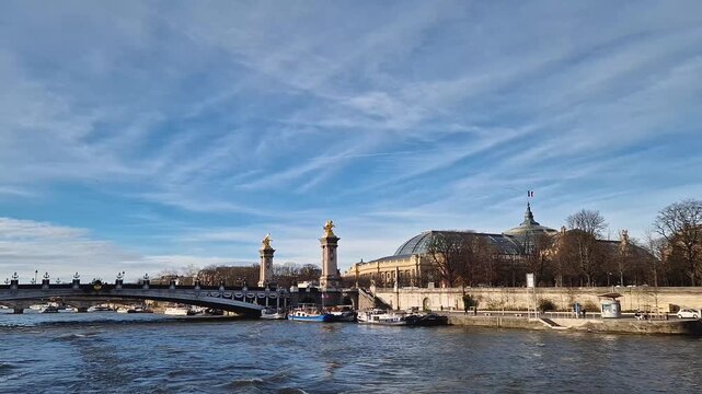 View from a cruising boat trip along the Seine river to the breathtaking Pont Alexandre III in Paris, France. The bridge is adorned with gilded statues. The Grand Palais with glass dome in background