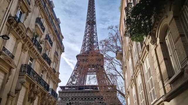 Low-angle view of the Eiffel Tower framed by elegant parisian residential buildings. The intricate iron lattice monument towering over classic Haussmann style facades with ornate balconies