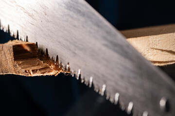Close-up of carpenters hand saw cutting wood board working in carpenter shop.