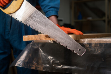 Close-up of carpenters hand saw cutting wood board working in carpenter shop.
