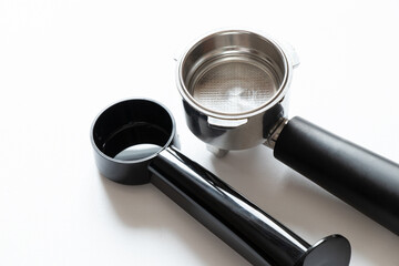 A metal coffee portafilter and measuring spoon on a white background