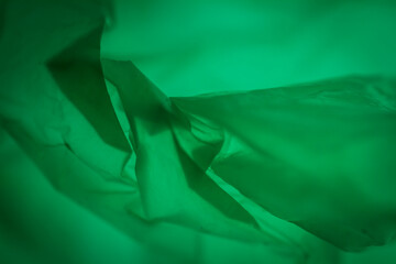 Extreme close up of green empty plastic bag background. The plastic surface is wrinkly and tattered making abstract pattern. Selective focus, shallow depth of field.