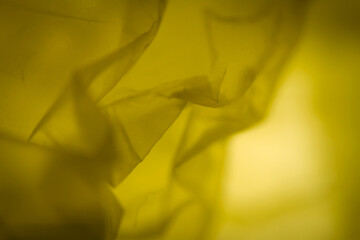 Extreme close up of yellow empty plastic bag background. The plastic surface is wrinkly and tattered making abstract pattern. Selective focus, shallow depth of field.
