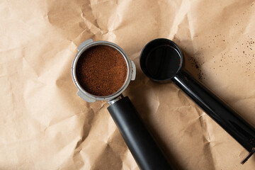 A metal coffee portafilter, measuring spoon, and loose coffee grounds lie on brown paper