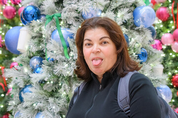 Woman playfully sticking out her tongue in front of a decorated Christmas tree.